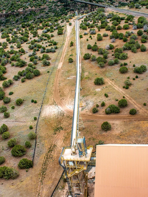 Aerial view of a long conveyor system at the Drake Cement facility in Paulden, Arizona, extending across desert terrain with surrounding vegetation.