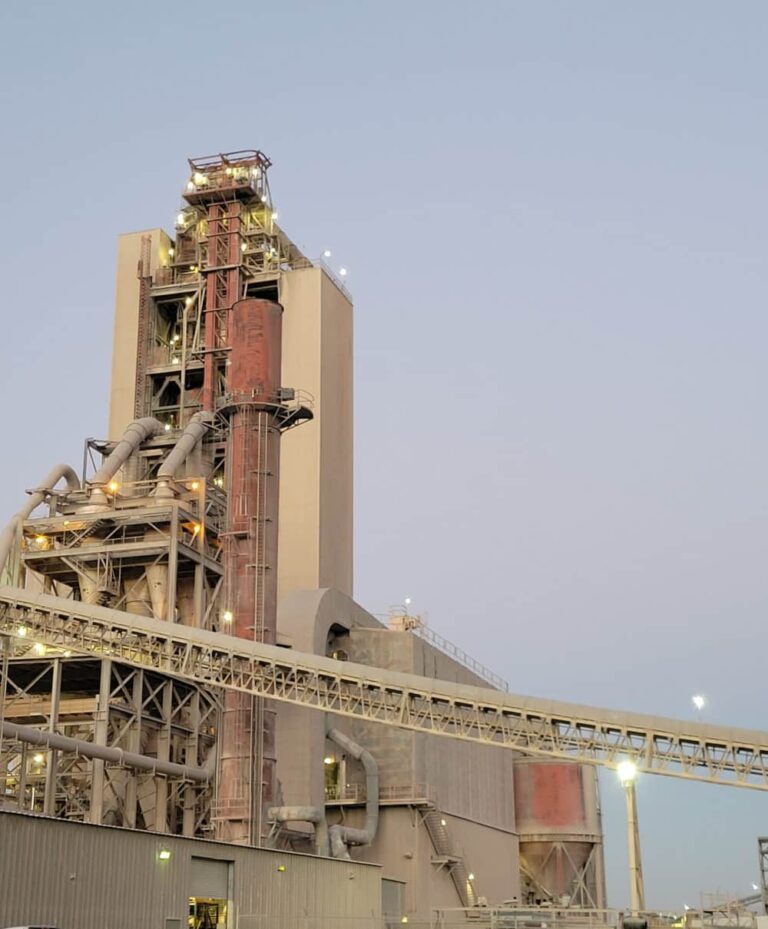 The Tehachapi Cement plant in California at dusk, showing illuminated industrial structures, towers, and material handling equipment.